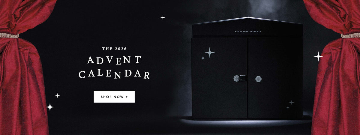 The 2026 Advent Calendar, shop now. Black Regalrose advent calendar box with closed doors, framed by red theatre curtains