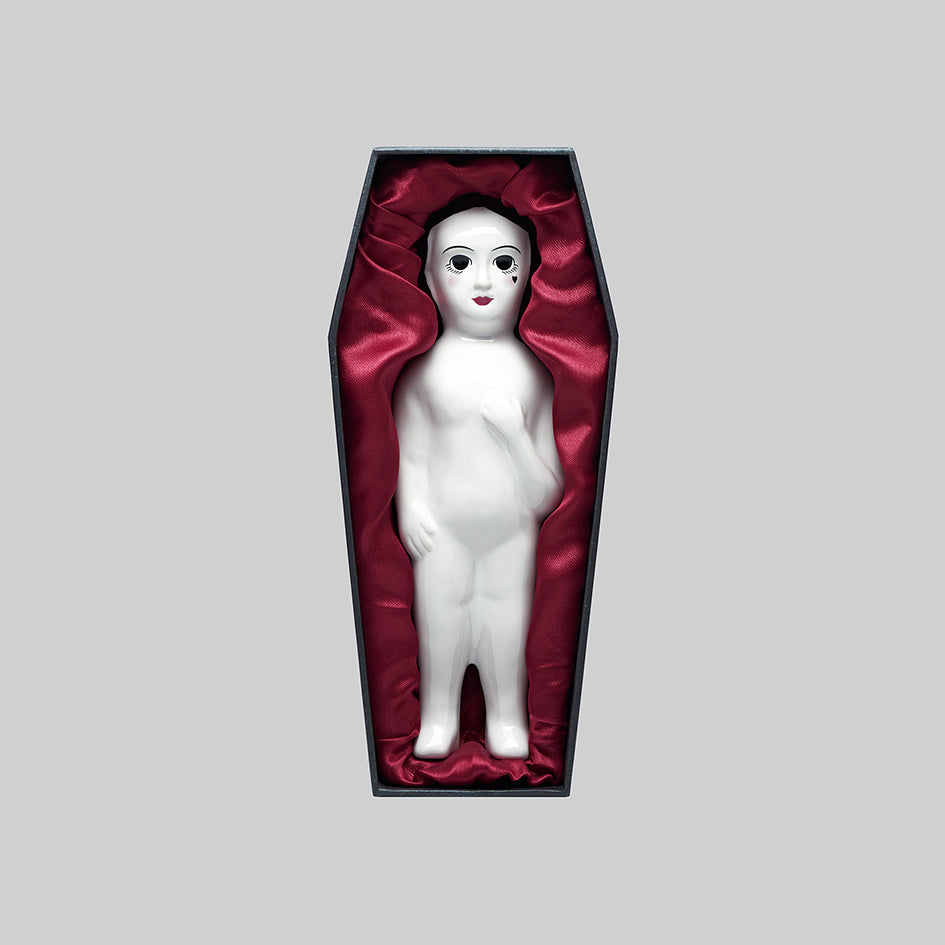 Regalrose Frozen Charlotte ceramic figurine lying in its coffin-shaped box lined with red satin, front view