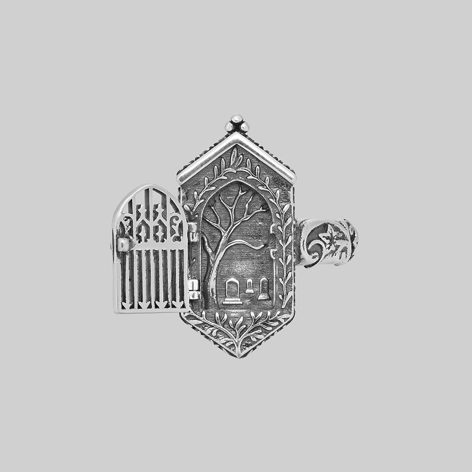 Silver iron gate ring open, revealing engraved tree and gravestones