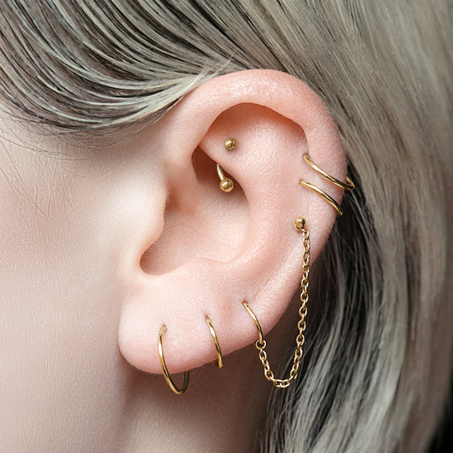 Close-up of an ear with gold earrings against a neutral background