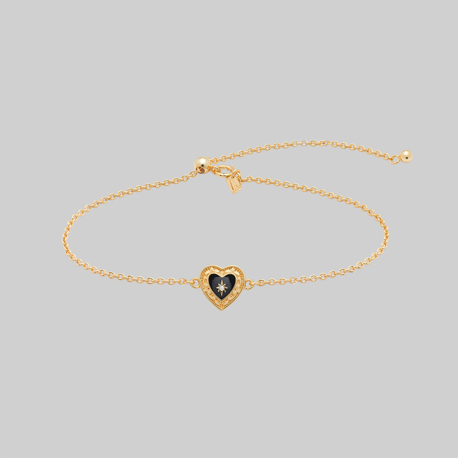 SOLEMN. Black Enamel Heart Bracelet - Gold Gold bracelet with a heart-shaped charm on a light gray background