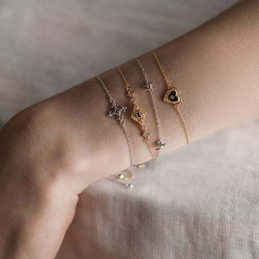 SOLEMN. Black Enamel Heart Bracelet - Gold Close-up of a wrist wearing multiple gold and silver dainty bracelets
