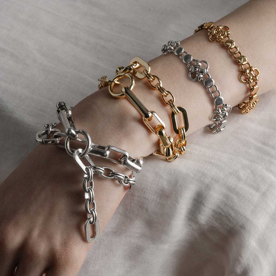 four chunky chain bracelets in gold and silver, worn on a models wrist