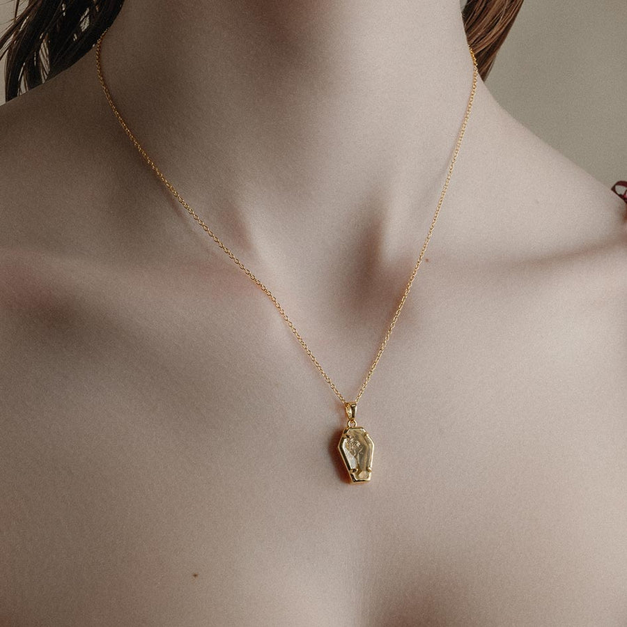 REBIRTH. Rose Under Glass Coffin Necklace - Gold Gold plated necklace with a glass rose coffin pendant on a person's neck
