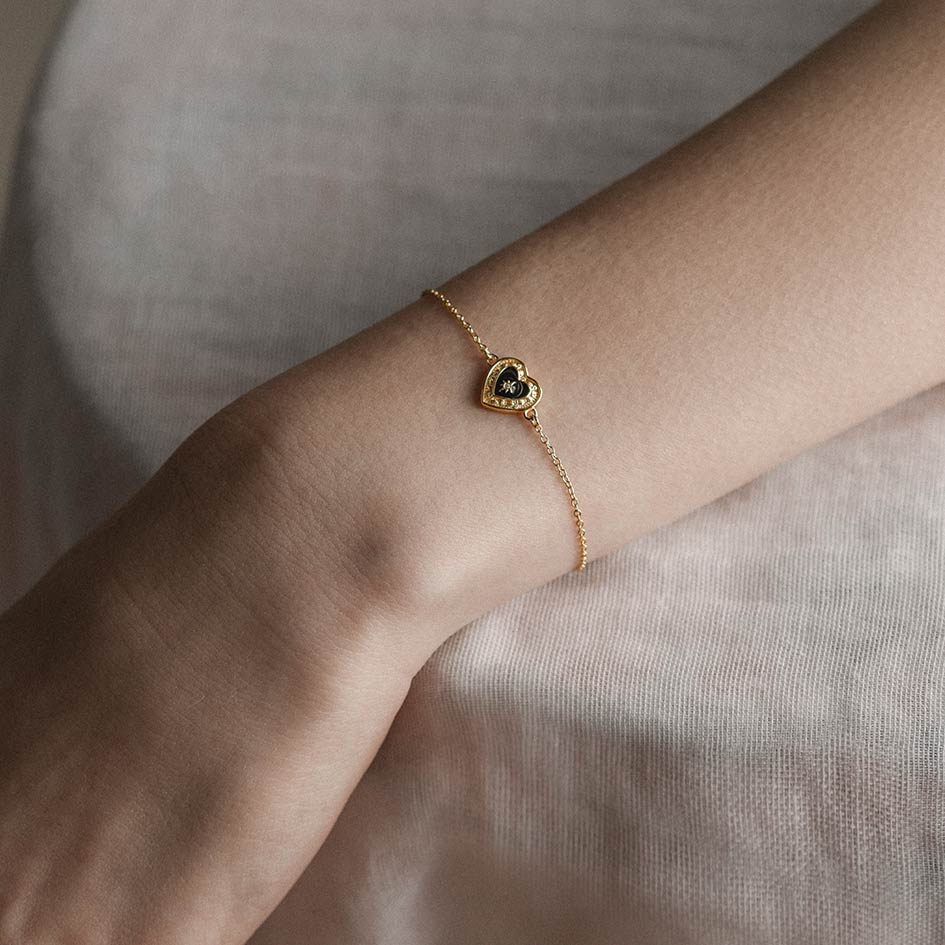 Gold bracelet with a heart-shaped clasp on a wrist against a neutral background