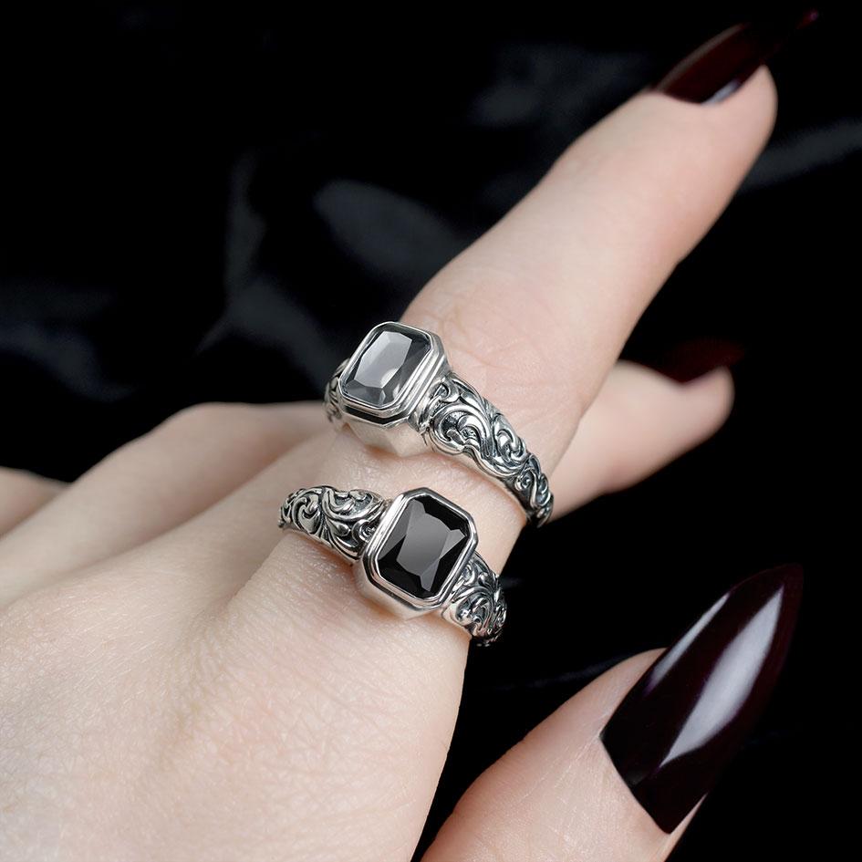 Two sterling silver signet style rings stacked together, each set with an emerald-cut stone and finished with ornate scroll engraved bands