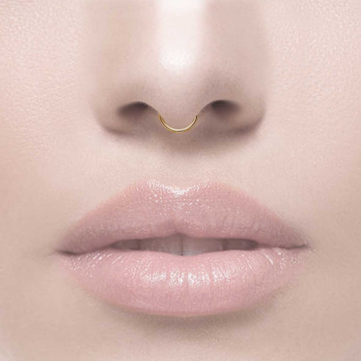 A small gold-colored septum clicker ring with a simple design, worn by model