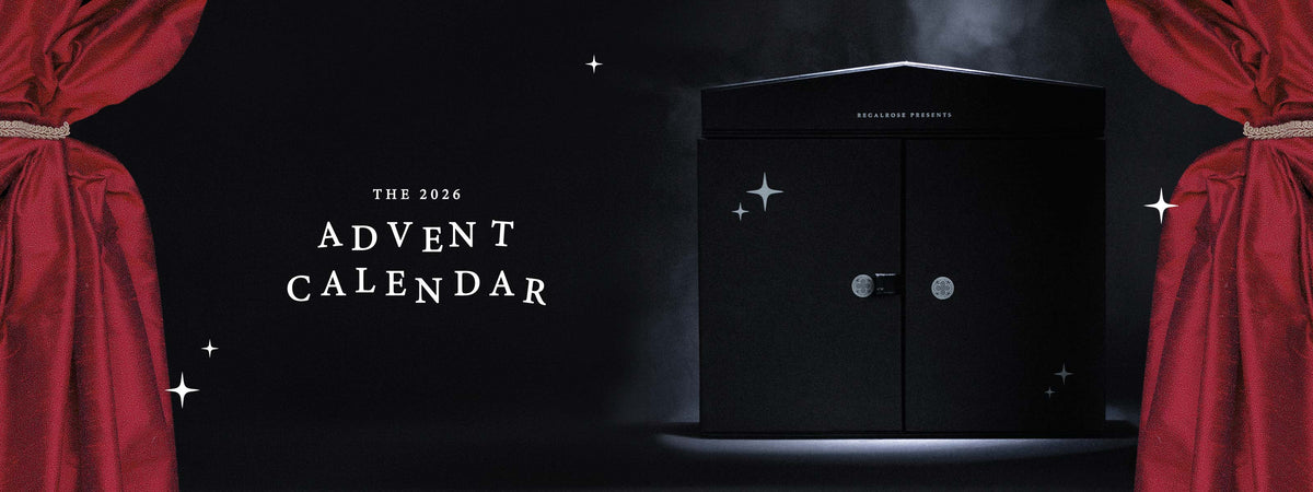 The 2026 Advent Calendar. Black Regalrose advent calendar box with closed doors and silver stars, framed by red theatre curtains