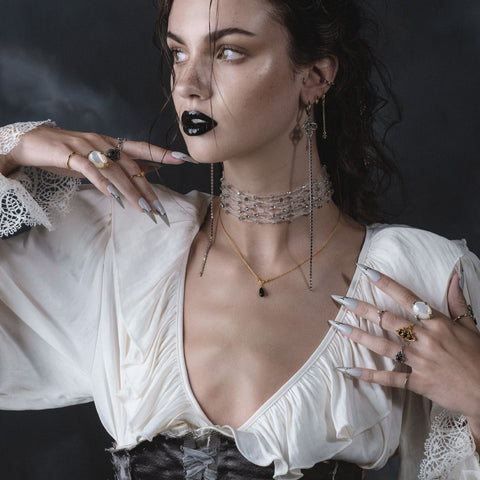 Model in cream blouse wearing layered beaded chokers, gold droplet necklace and stacked rings