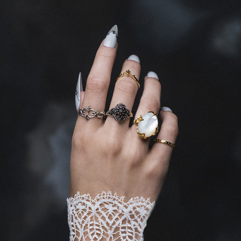 Close-up of hand wearing stacked gold and silver rings with pearl and black onyx stones