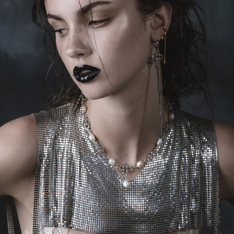 Model in silver chainmail top wearing pearl and chain collar with long beaded earrings