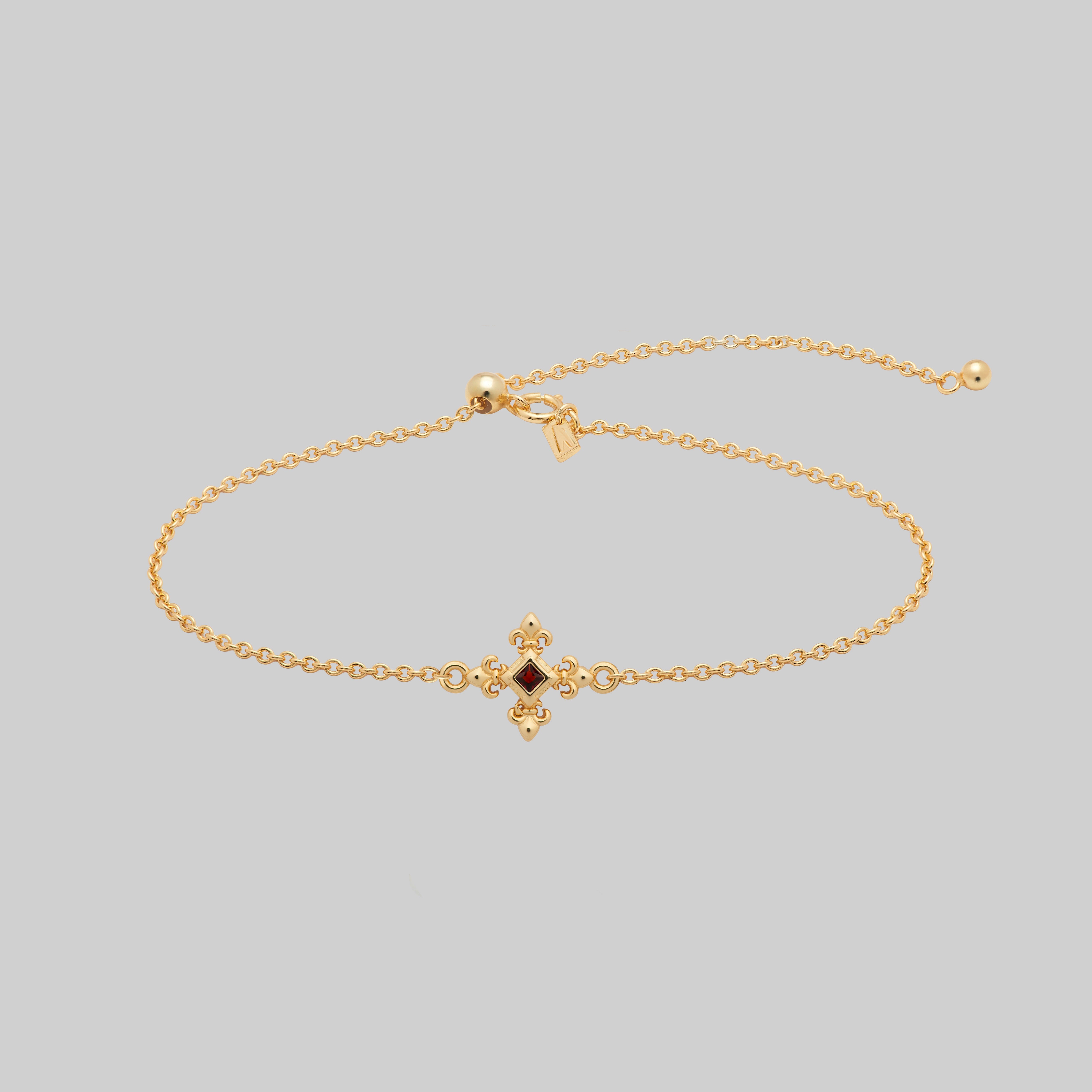Gold dainty bracelet with a central garnet gemstone and decorative clasp