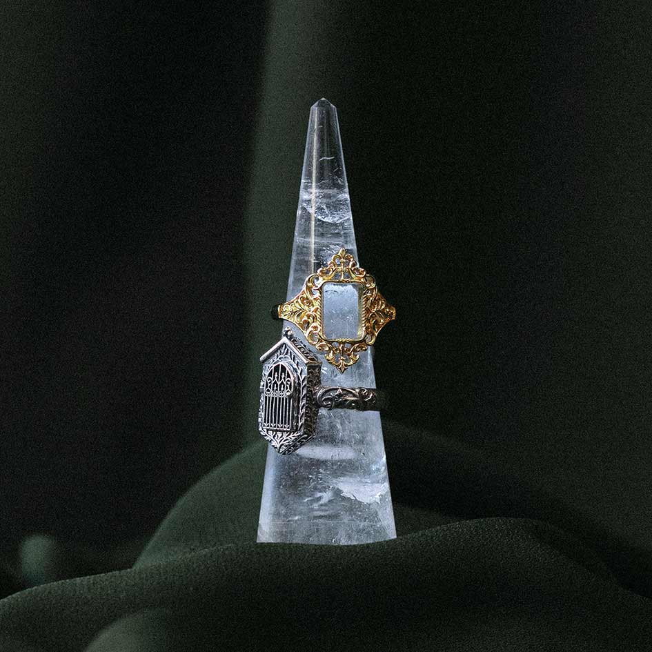 Ornate frame ring and gothic gate ring displayed on a clear quartz point against velvet.