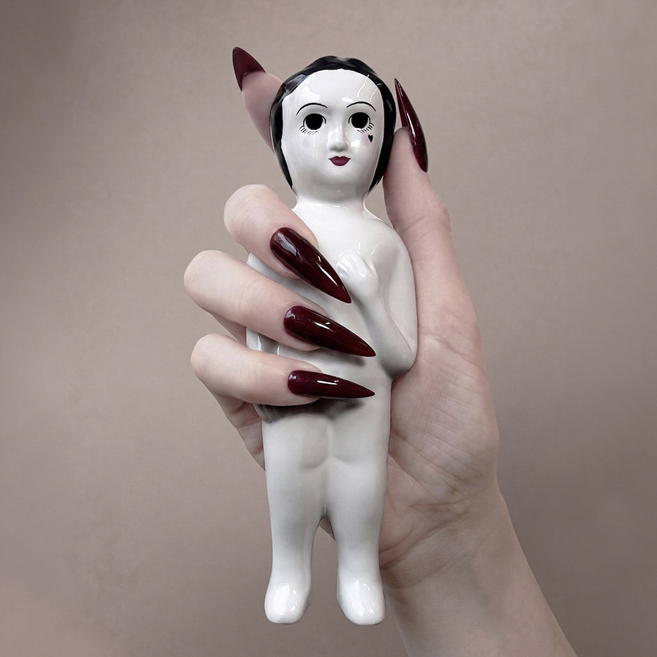 Hand holding a small white figurine with black hair 