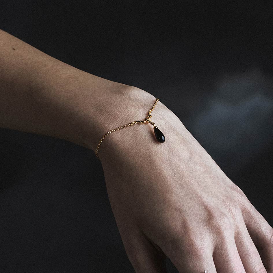 Model wearing Lisette gold heraldic lily black glass droplet bracelet