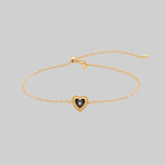 Gold bracelet with a heart-shaped charm on a light gray background
