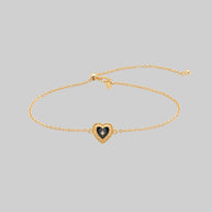 Gold bracelet with a heart-shaped charm on a light gray background