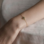 Gold bracelet with a heart-shaped clasp on a wrist against a neutral background
