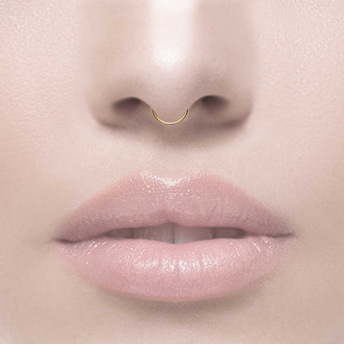 A small gold clicker ring with a simple design worn by model as a septum piercing